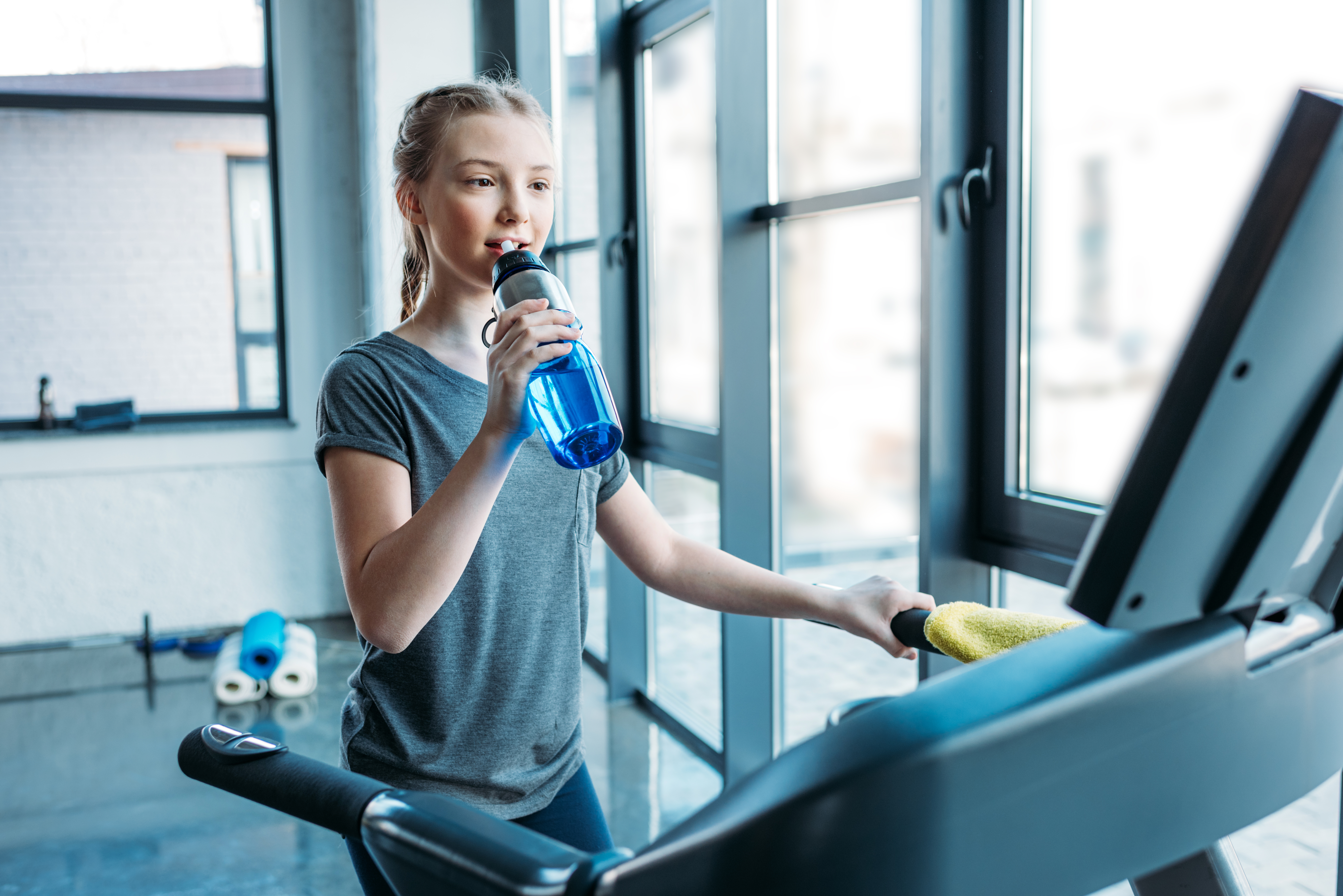 Preteen,girl,training,on,treadmill,and,drinking,water,in,fitness